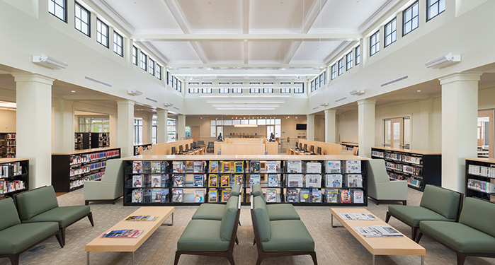 photo of the inside of the library picturing a seating area with several chairs, the magazine and newspaper stands, the computer area, and some of the audio book and CD shelves