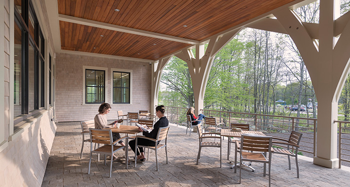 A photo of the library's patio with several sets of tables and chairs with three women sitting and reading at them