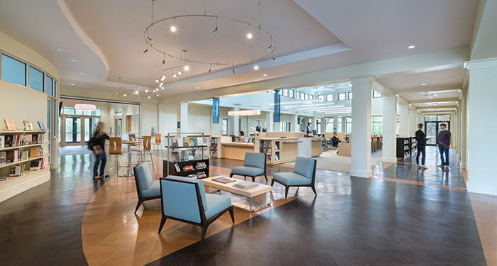 picture of the inside of the tiverton public library picturing a seating area, the check out desk and several people using the library