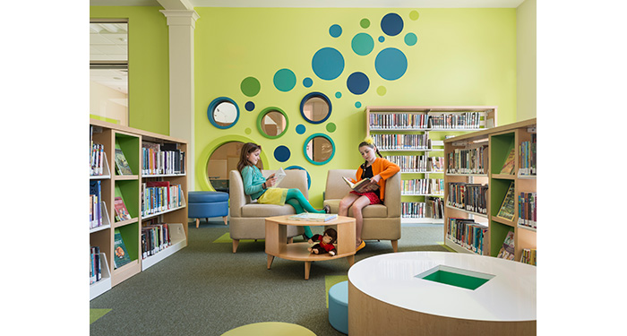 two girls sitting in chairs and reading in the fiction section inside of the children's room