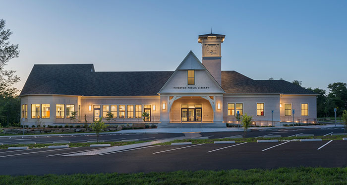 photo of the tiverton public library at night with all of the lights shining through the windows